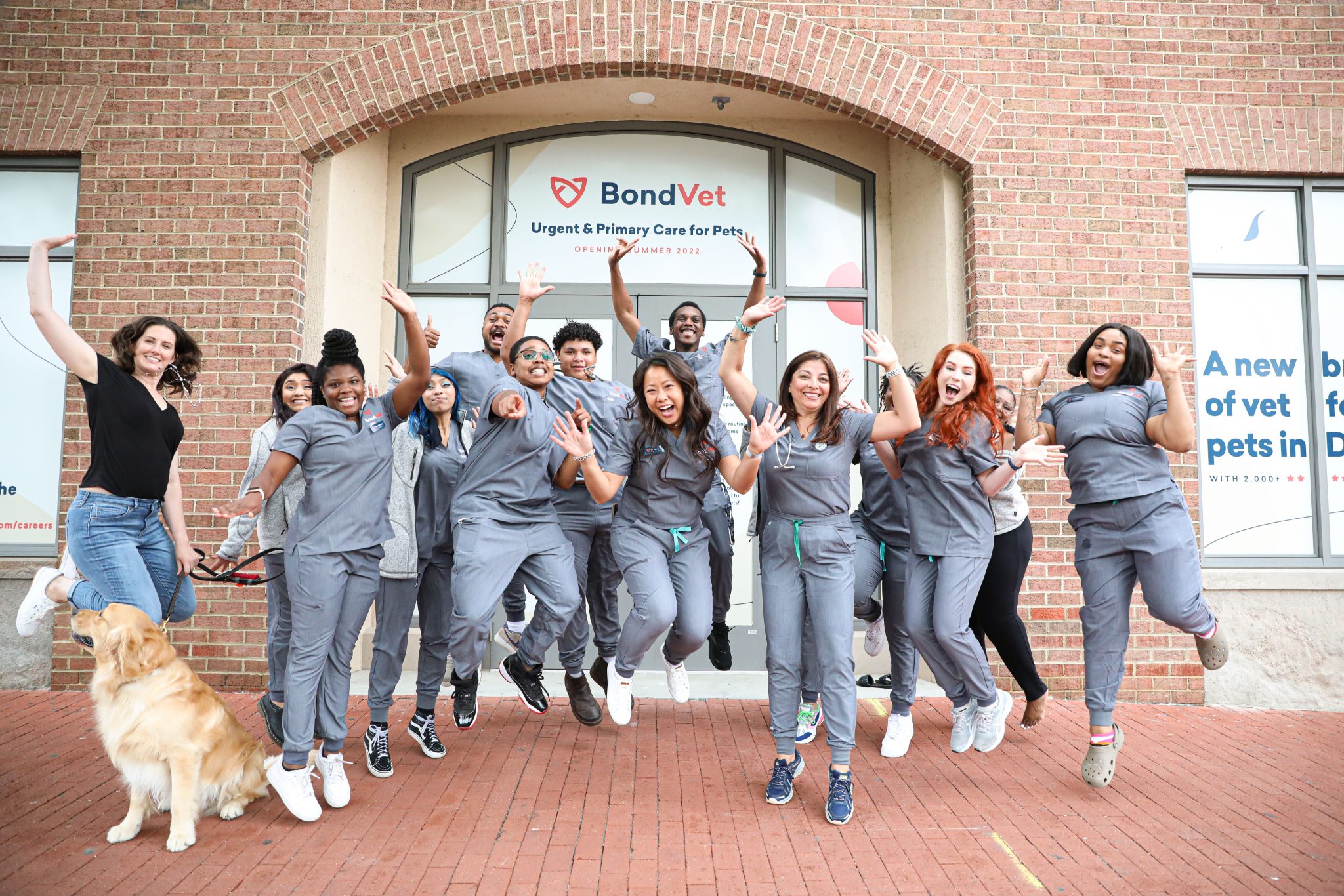 Happy Bond Vet employees, in their blue scrubs, jumping in the air outside of the new office