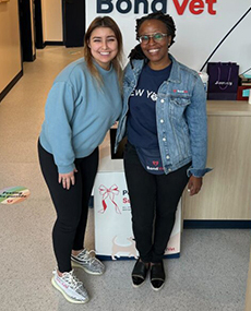 Two Employee staff standing in front of the Bond Vet logo in a clinic, smiling